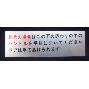 画像: プレート　「非常の場合は、この下の赤わくの中のハンドルを手前に引いてくださいドアは手であけられます」」